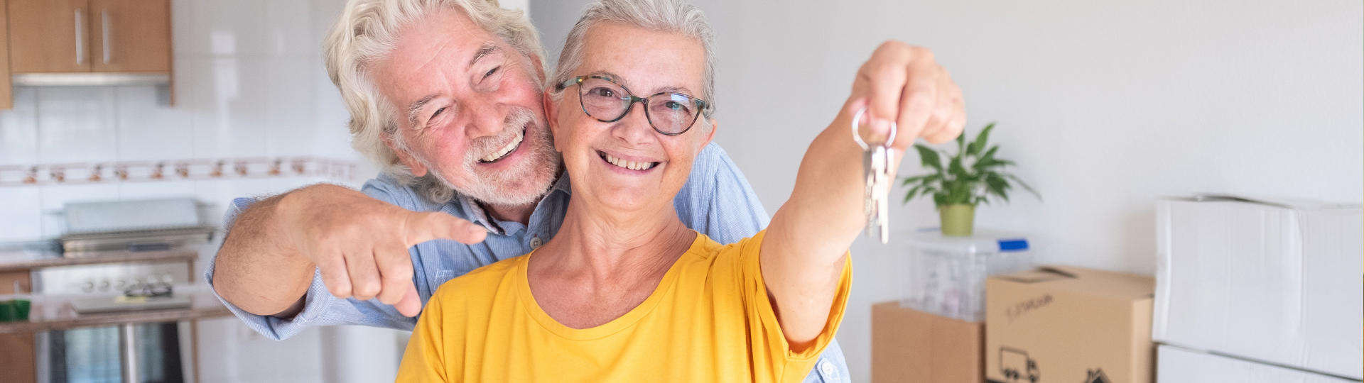 A senior man and woman smile while holding keys to their new home