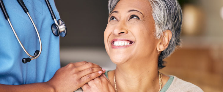 A senior woman smiles up at a nurse